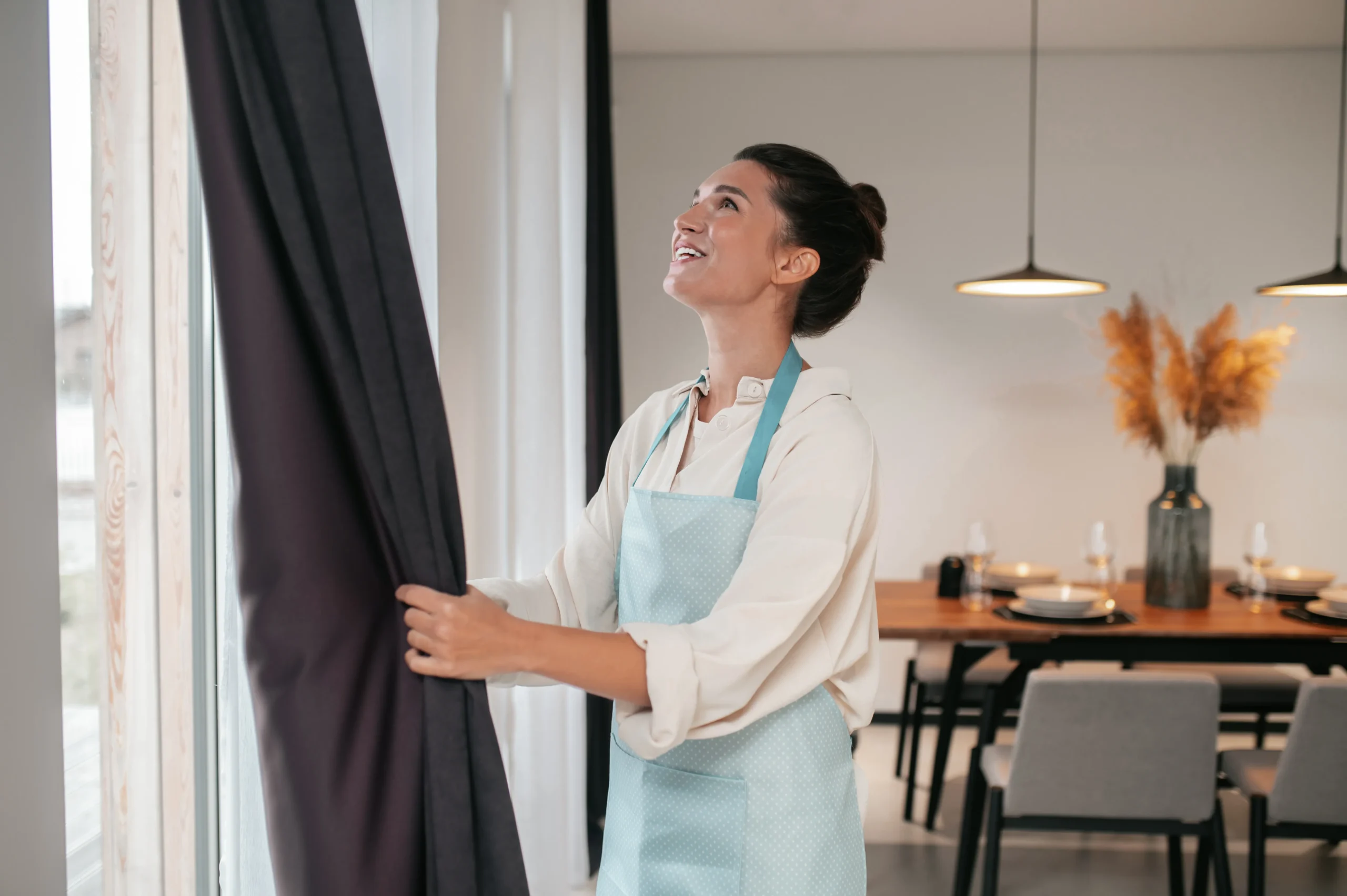young woman standing near widnow fixing curtains.jpg scaled